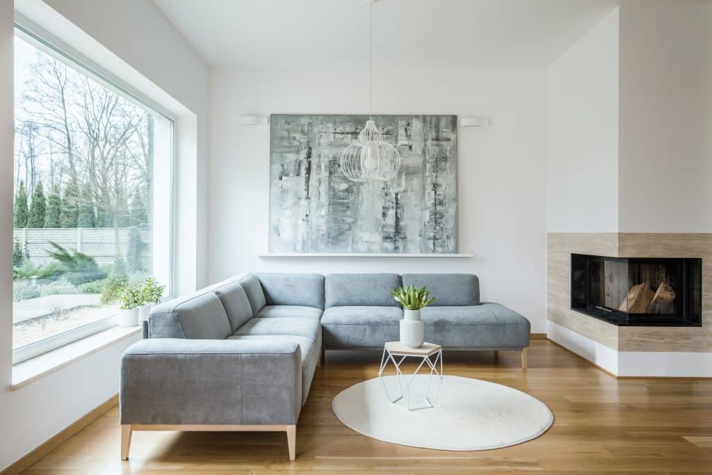 Chimenea junto a un sofá de esquina gris y mesa con tulipanes contra la pared blanca con la pintura en el interior del apartamento