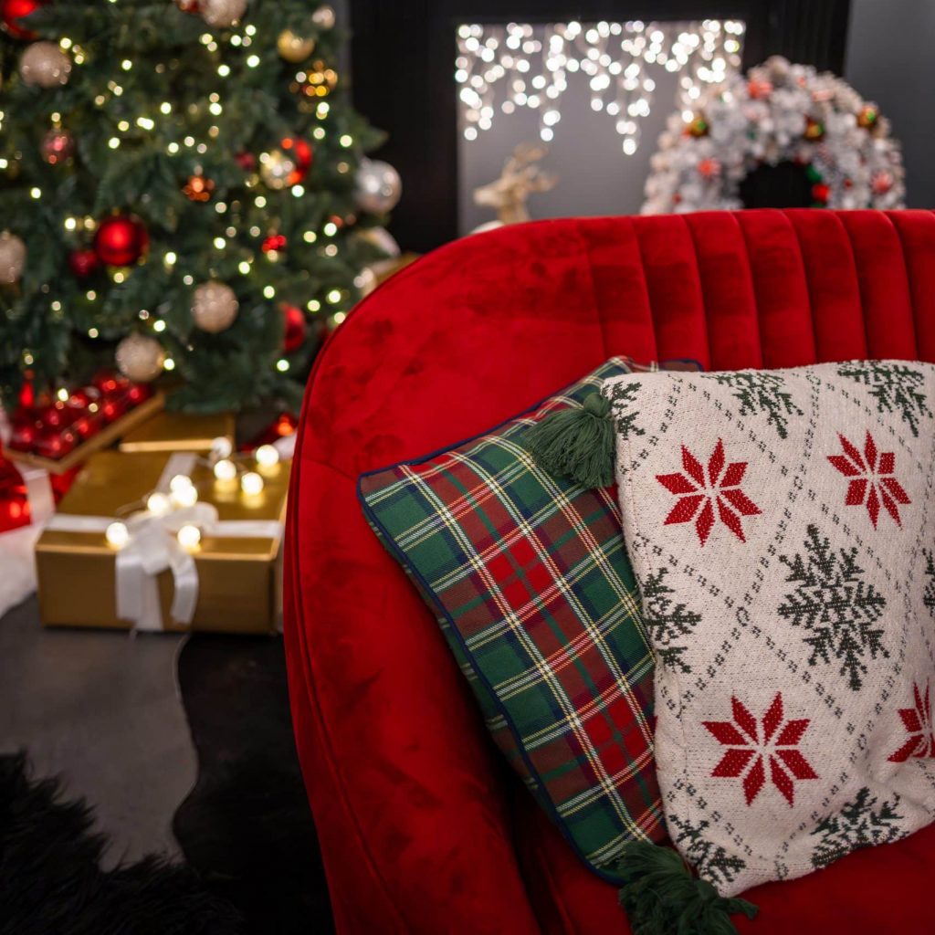 Sofá de terciopelo con árbol de Navidad y cojines decorativos en tonos rojos y verdes suaves.