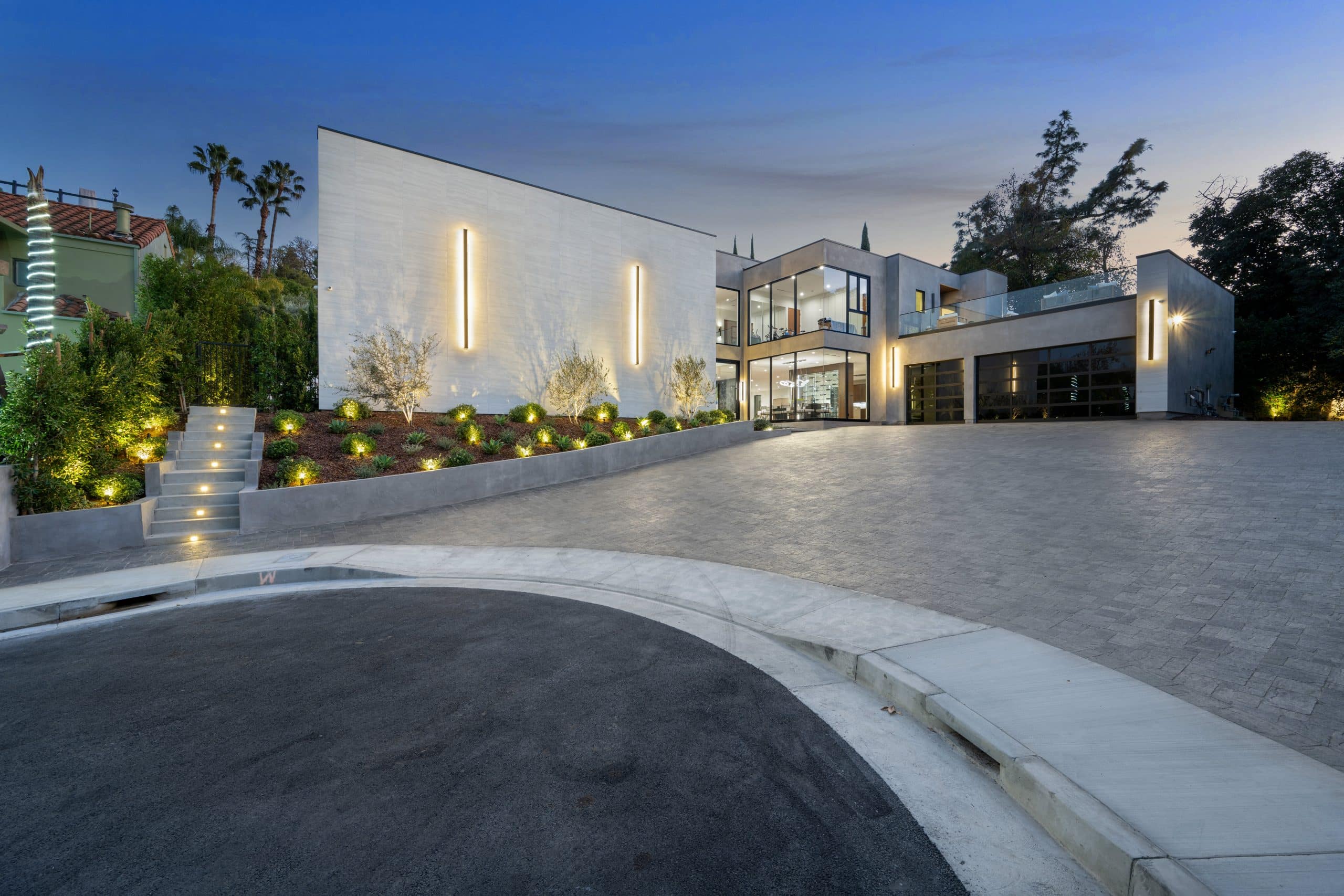 Lujosa villa de estuco y hormigón con elegantes luminarias en el patio y una gran entrada principal