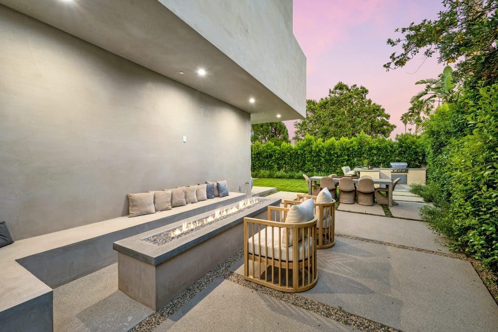 Mesa y sillas de exterior en un patio con vegetación verde al fondo.